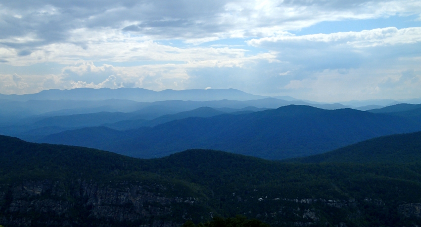 A. vast mountain range appears in shades of blue under a blue sky with clouds.